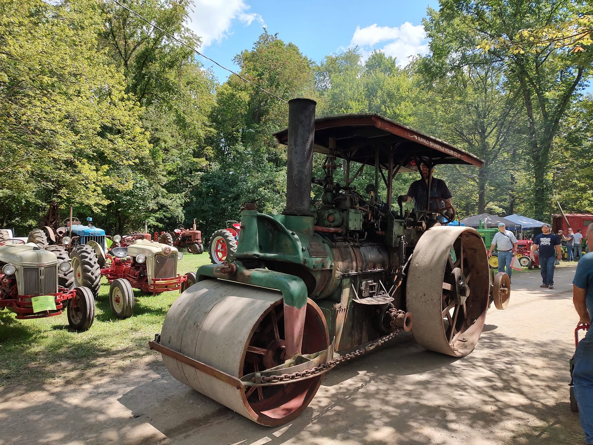 Green Buffalo-Springfield steam road roller moving through the showgrounds with tractors behind it